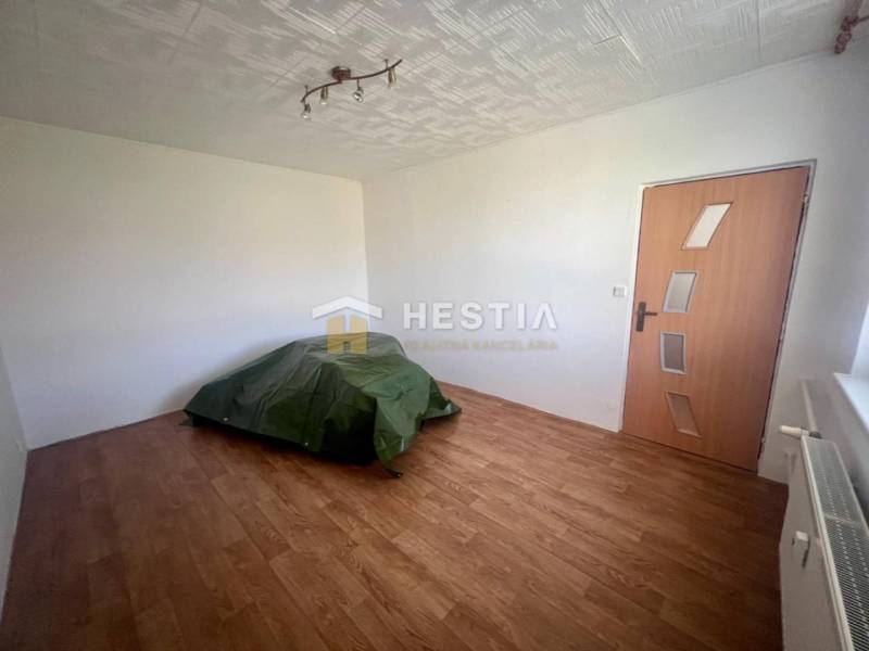 Soba u trojizbovom byte s podlahom, radiátorom, dverima i jednostavnim osvetljenjem.