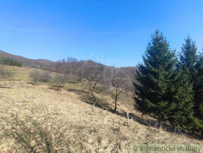 Dombos táj Új Bánya közelében, kertekkel, füves területekkel és fákkal.