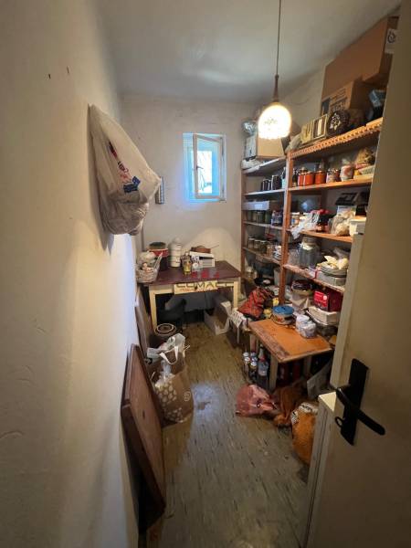 Családi ház tárolóhelyisége polcokkal, amelyek tele vannak különféle tárgyakkal és nyitott ablakkal.