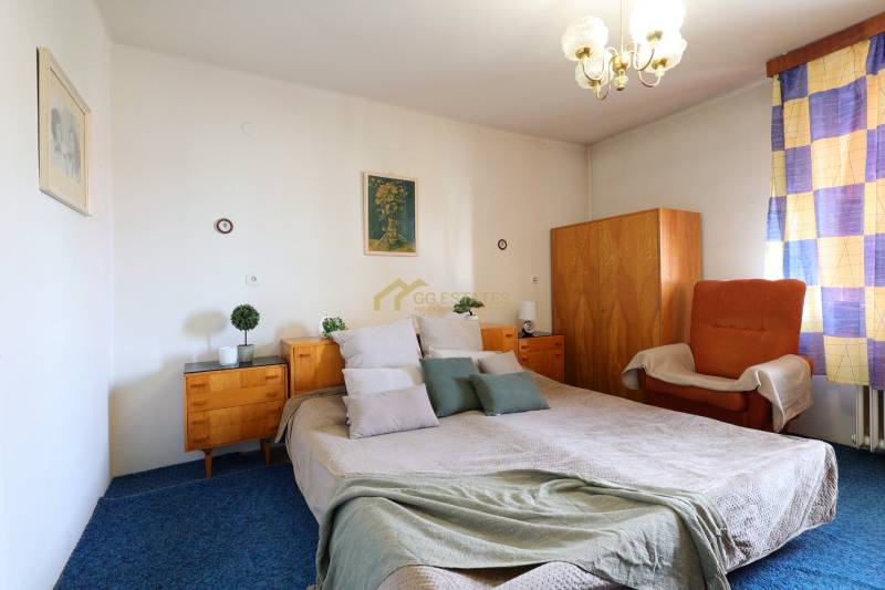 Hálószoba nagy ággyal, fa szekrényekkel és székkel egy családi házban.