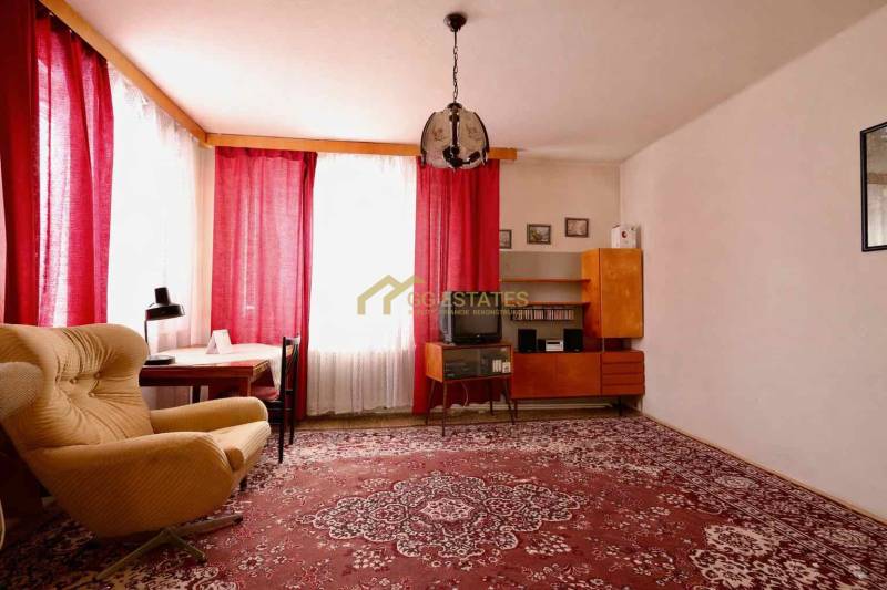 Nappali egy családi házban, piros szőnyeggel, fotellel és függönyökkel az ablakokon.