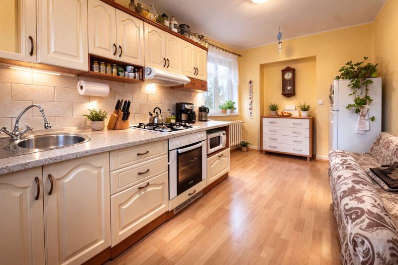 Konyha egy kétszobás lakásban fa mintázatú padlóval, világos konyhabútorral és növényekkel.