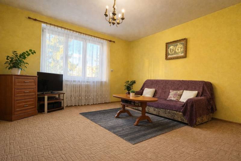 Nappali egy kétszobás lakásban, sárga falakkal, szőnyeggel és bútorokkal.