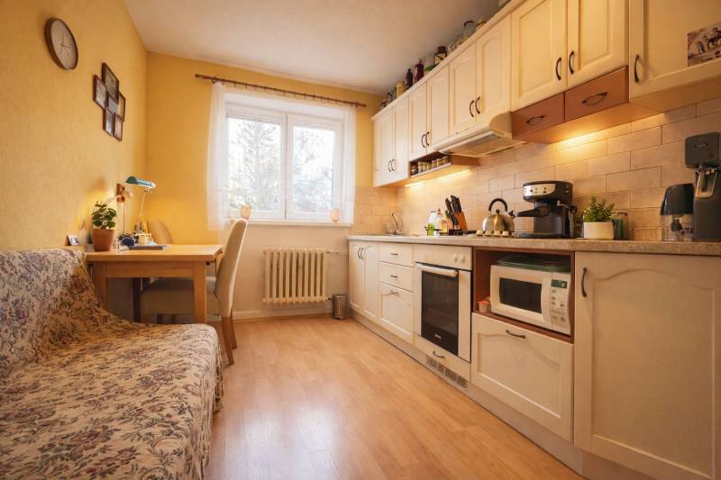 Konyha egy kétszobás lakásban, fa dekor padlóval, világos bútorokkal és étkező sarokkal.