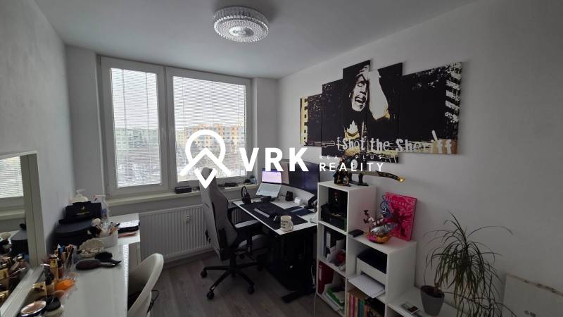 Dolgozószoba egy háromszobás lakásban, asztallal, polccal, képpel és fa dekorációjú padlóval.