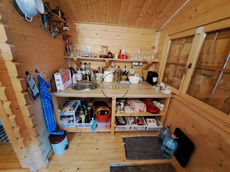 Fa konyha készülékekkel, polcokkal és mosogatóval a kert belsejében.