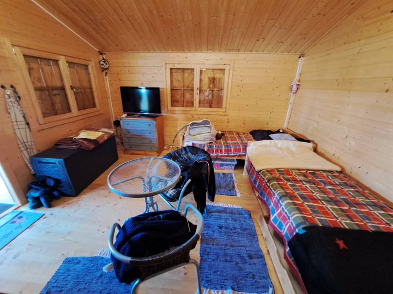 Szoba a kertekben asztallal, székekkel és két ággyal színes takarókkal.