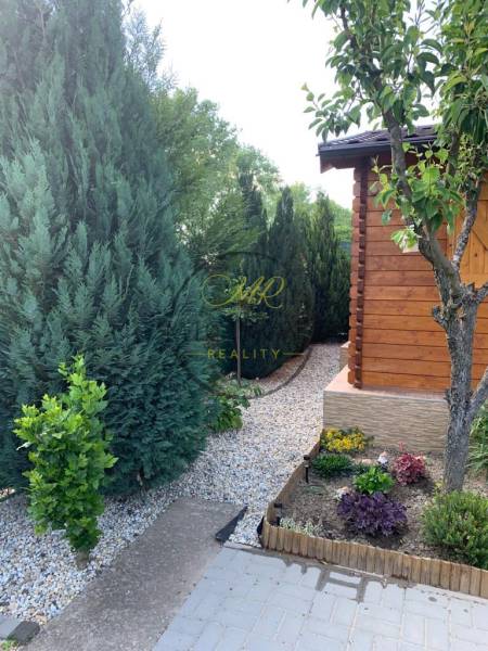 Kertek Alsókrškánban, Nyitra, gondozott tűlevelűekkel és egy fából készült kerti házzal.