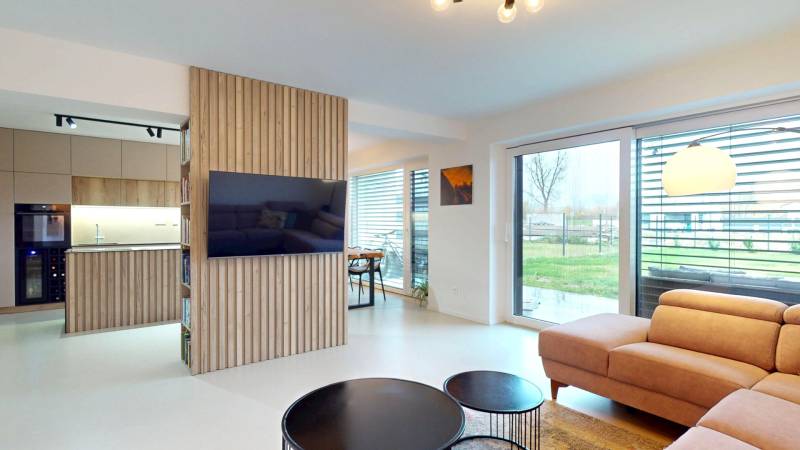 Nappali nagy ablakokkal, kényelmes kanapéval és fa dekorációval a falon.