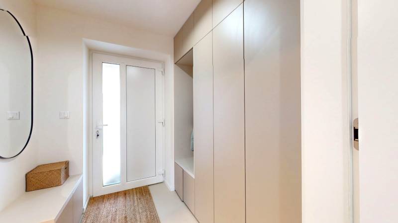 Családi ház előszobája akasztós szekrénnyel, tükörrel és szőnyeggel.