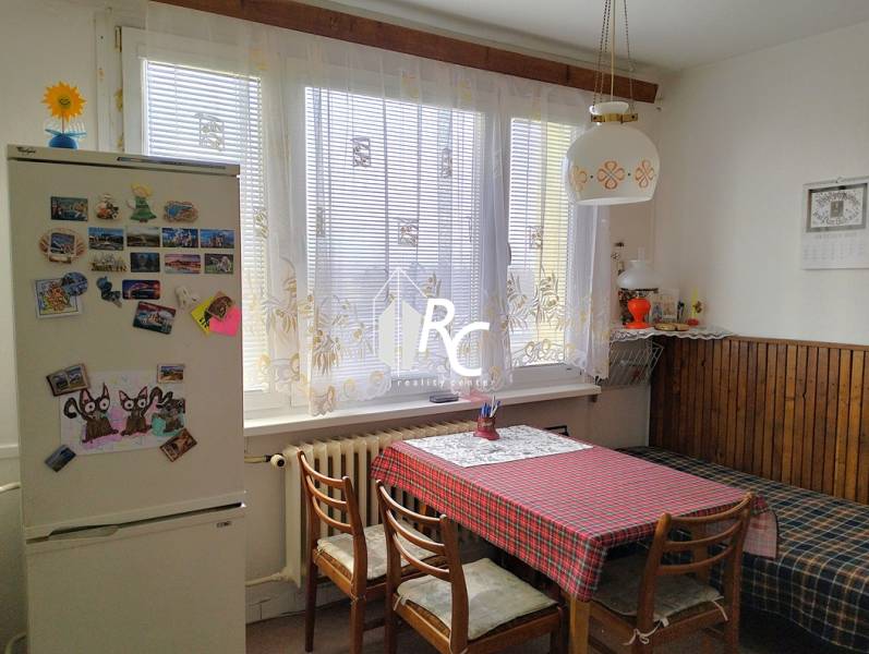 Konyha egy kétszobás lakásban étkezőasztallal, székekkel és hűtőszekrénnyel, amelyen mágnesek vannak.