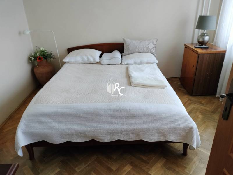 Hálószoba franciaággyal, fa mintázatú padlóval és éjjeliszekrénnyel egy kétszobás lakásban.