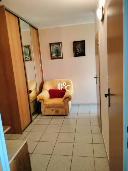 Szék a bejárati ajtónál csempézett padlóval egy kétszobás lakásban, tükrös szekrény.