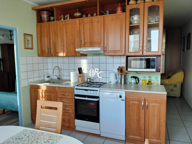 Konyha egy kétszobás lakásban fa dekorációval, felszerelve háztartási gépekkel és tárolóhellyel.