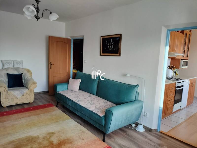 Nappali egy kétszobás lakásban kanapéval és fotellel, fa dekoros padlóval.