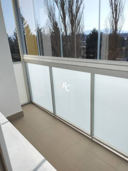 Üvegezett erkély egy kétszobás lakásban, kilátással a fákra és a hegyekre.