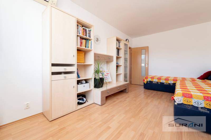 Egy fa dekoros padlóval rendelkező szoba, amely bútorokat, polcokat, egy franciaágyat és színes takarót tartalmaz.