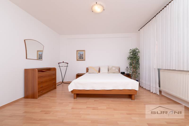 Hálószoba ággyal, komóddal és fa dekorációjú padlóval egy háromszobás lakásban.