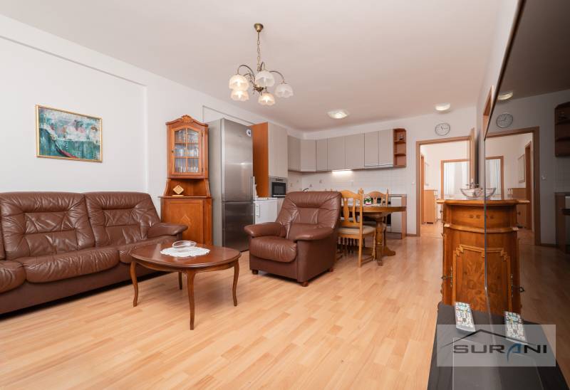 Nappali bőrkanapéval, étkezőasztallal és konyhával, 3 szobás lakás, fa dekoros padlóval.