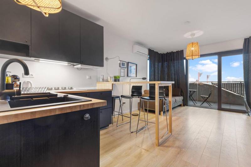 Konyha fekete szekrényekkel, bárpulttal és fa dekorációjú padlóval egy egyszobás lakásban.