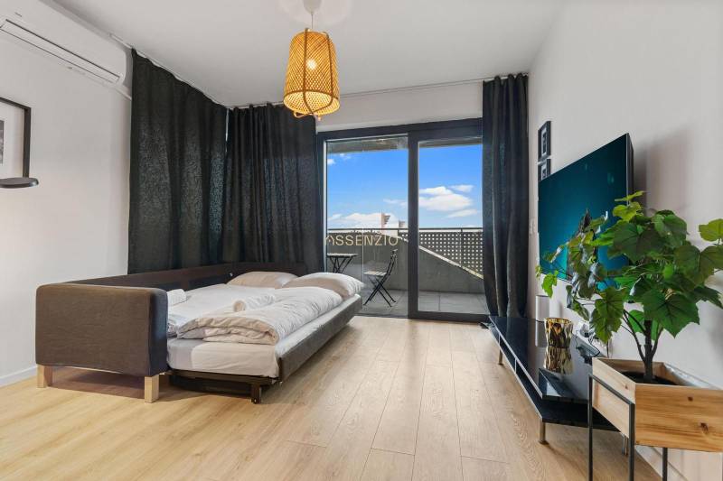 Nappali rész egy egyszobás lakásban ággyal, fa dekoros padlóval és erkéllyel.