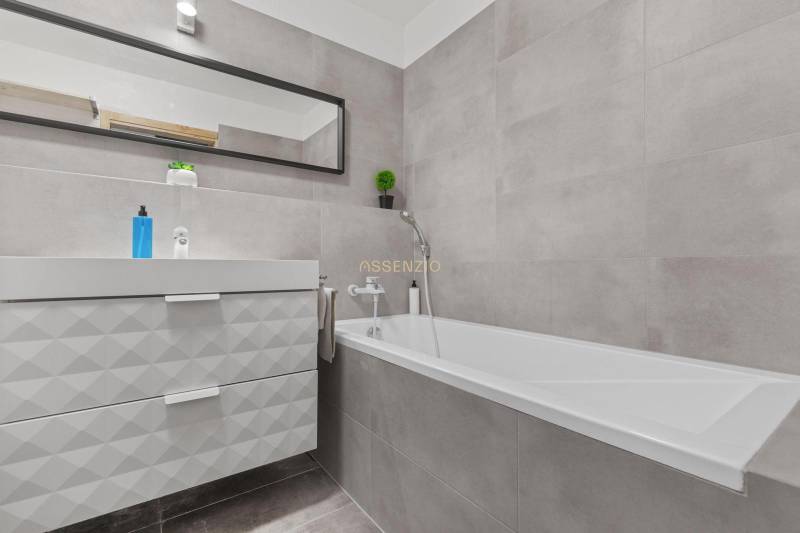 Fürdőszoba káddal, mosdóval és tükörrel egy egyszobás lakásban.