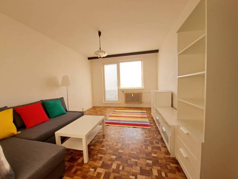 Nappali egy kétszobás lakásban kanapéval, fehér bútorokkal, színes párnákkal és fa dekorációjú padlóval.