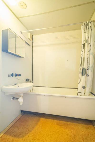 Fürdőszoba káddal és zuhanyfüggönnyel egy kétszobás lakásban, világos falak, narancssárga padló.