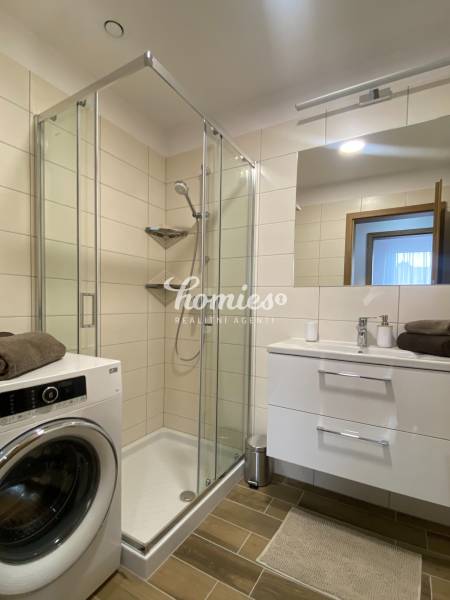 Fürdőszoba egy kétszobás lakásban mosógéppel, zuhanyzóval és fa dekorációjú padlóval.