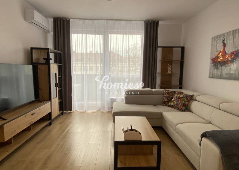 Nappali egy kétszobás lakásban, fa dekoros padlóval, világos kanapéval és televízióval.