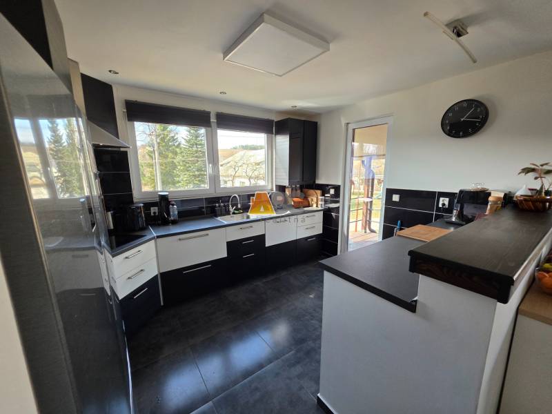 Konyha egy családi házban kerámia padlóval, sötét bútorokkal és nagy ablakokkal.