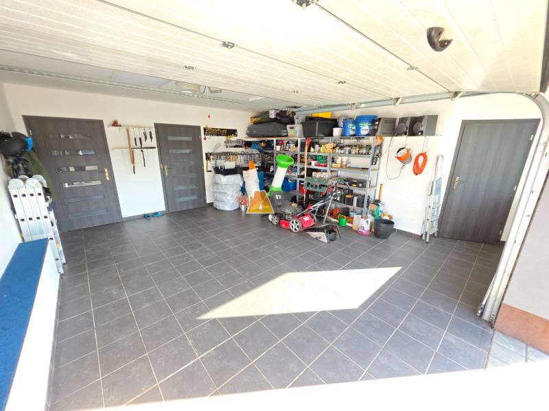 Családi ház garázsa szerszámokkal és tároló polcokkal, kerámia csempével burkolt padló.