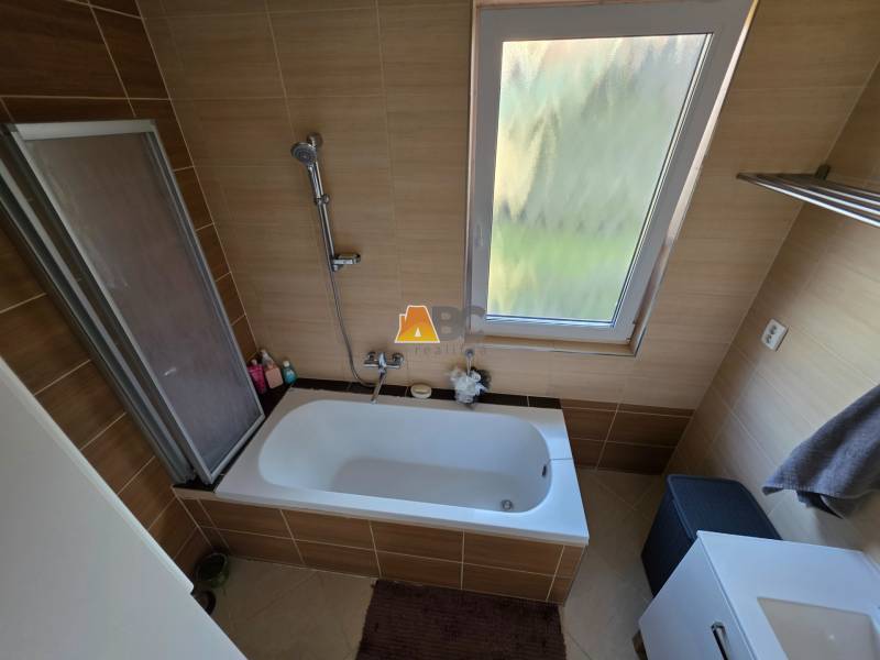 Fürdőszoba családi házban káddal és ablakkal, barna csempével burkolva.