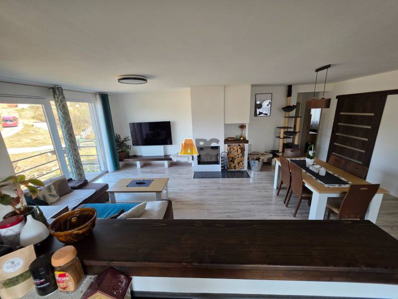 Nappali egy családi házban kanapéval, televízióval és étkezőasztallal, fa dekor padlón.