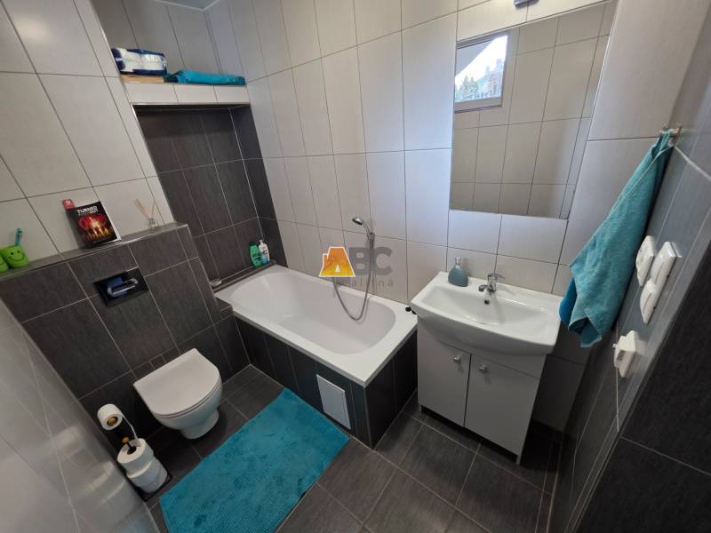 Fürdőszoba családi házban káddal, mosdóval és WC-vel, sötét mintázatú csempével.