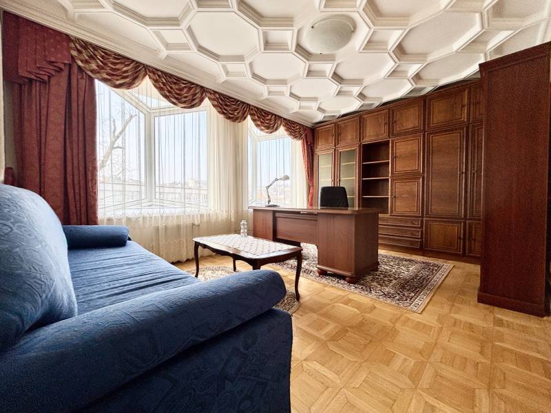 Szoba egy 4 szobás lakásban kényelmes kanapéval, íróasztallal és fa dekorációjú padlóval.