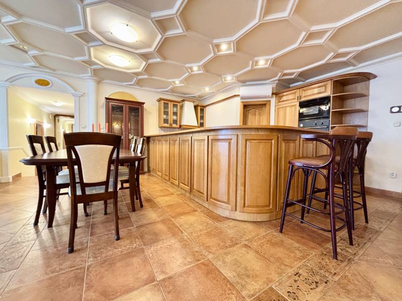 Konyha egy 4 szobás lakásban, étkezőasztallal, fa bútorokkal, csempével és érdekes mennyezettel.