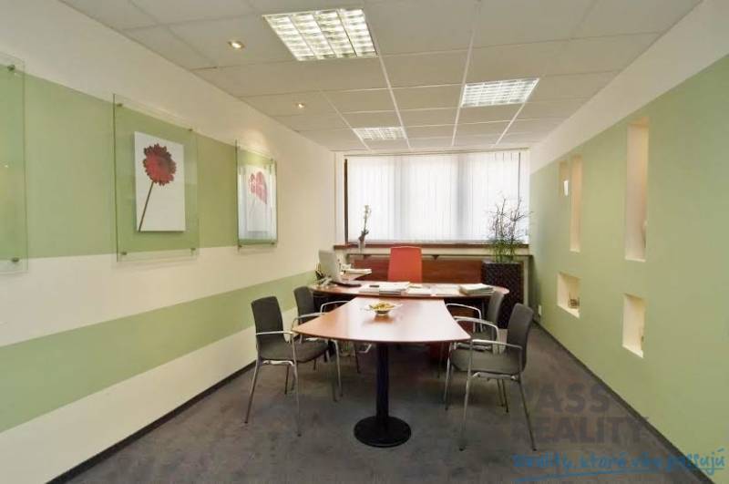 Irodák íróasztallal, székekkel, falakon elhelyezett dekorációkkal és ablakkal, függőleges redőnyökkel.