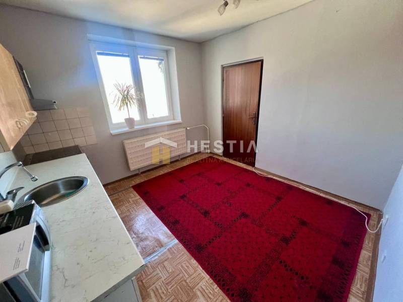 A háromszobás lakás konyhája szőnyeggel, fa dekor padlóval és egyszerű berendezéssel.