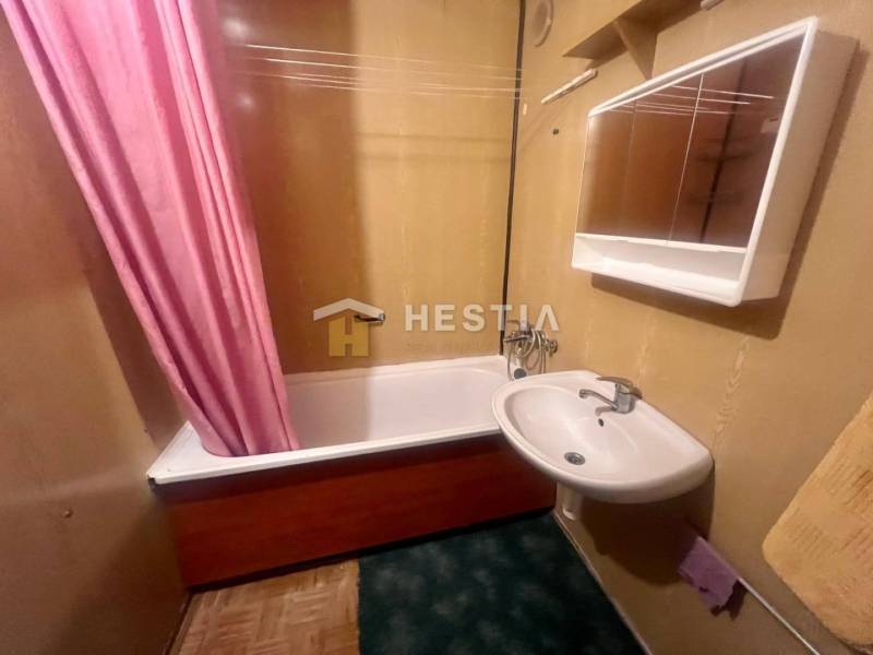 Fürdőszoba mosdóval és káddal egy háromszobás lakásban, a rózsaszín függöny hangsúlyos elemet ad hozzá.