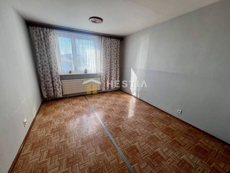 Szoba egy háromszobás lakásban, fa dekoros padlóval és világosszürke falakkal.