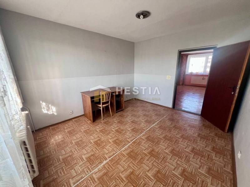 Szoba egy háromszobás lakásban, fa mintázatú padlóval és egyszerű íróasztallal.