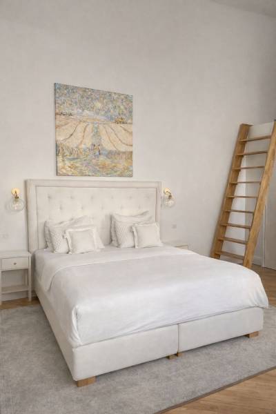 Világos hálószoba ággyal, falon lévő képpel, éjjeliszekrénnyel és fa dekorációjú padlóval.