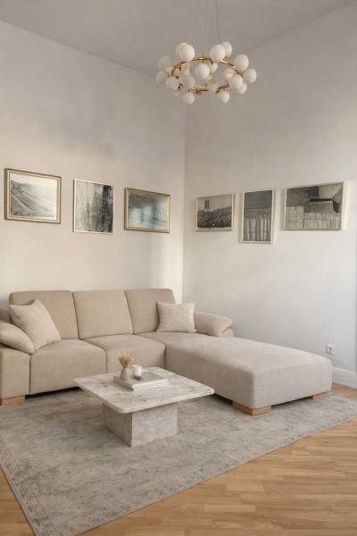 Nappali egy háromszobás lakásban bézs kanapéval, asztallal, képekkel és fa dekorációjú padlóval.