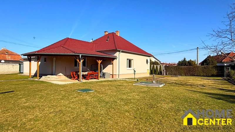 Családi ház Zemianska Olčán piros tetővel és fa előtetővel, füves kert.