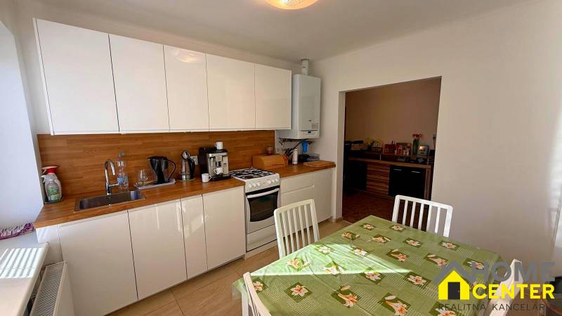 Konyha családi házban fehér szekrényekkel, fa dekorációval és étkezőasztallal.