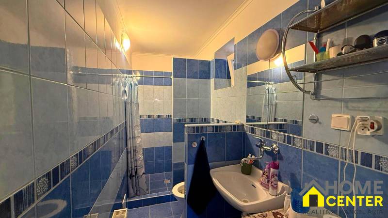 Fürdőszoba egy családi házban kék-fehér csempékkel, mosdóval és zuhanyzóval.