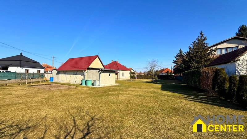 Gyepes telek családi ház mellett Zemianska Olčán, néhány házzal és bokorral.