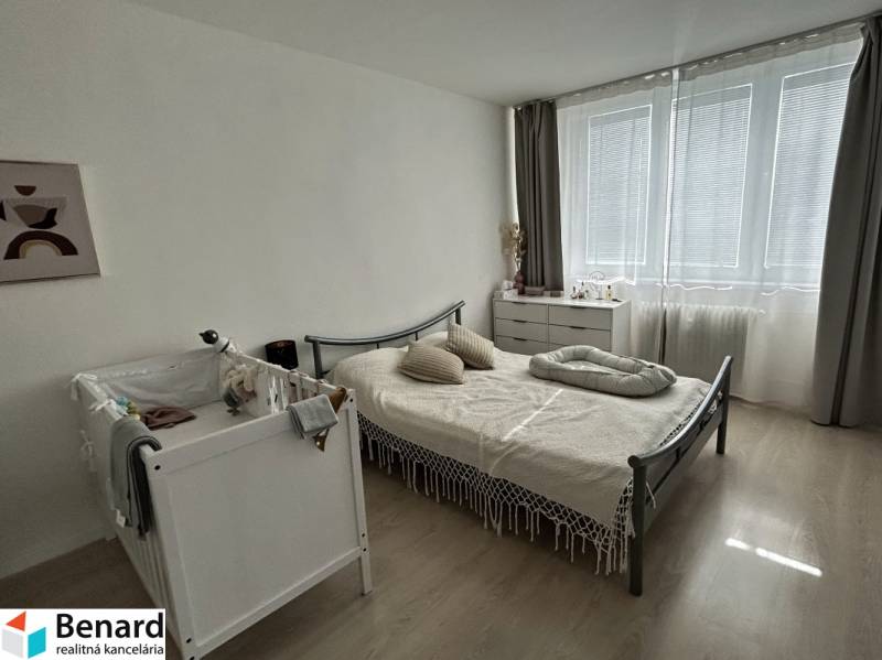 Hálószoba egy kétszobás lakásban kisággyal, ággyal és komóddal, fa mintázatú padlóval.