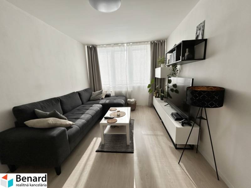 Nappali kanapéval, televízióval és fa mintázatú padlóval egy kétszobás lakásban.